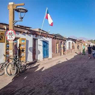 Calle Caracoles, la calle principal del pueblo de San Pedro de Atacama en Chile, con casas de adobe, banderas chilenas y ambiente turístico típico del desierto.